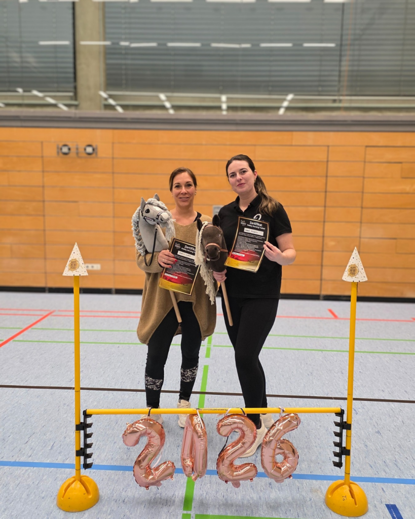 Steffi und Leoni, zertifizierte Hobby Horsing Trainerinnen des DtHHv beim RC Mauritius Diepersdorf, mit Steckenpferden und Trainerzertifikaten in der Sporthalle